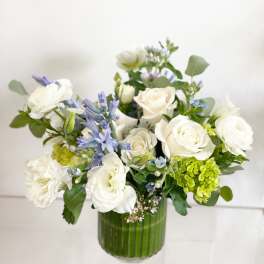 White roses and blue flowers in a green glass vase