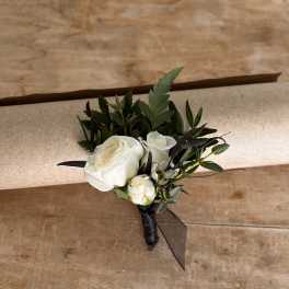 White rose boutonniere with dark greenery and black ribbon