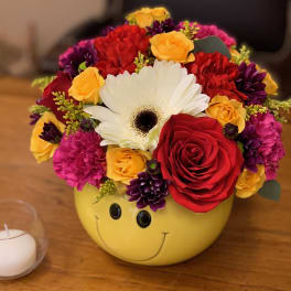 Colorful mixed flower arrangement in a yellow smiley-face container