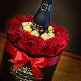 Red roses and gold chocolates arranged around a champagne bottle in a black box