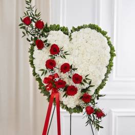 Heart-shaped white floral standing wreath with red roses on an easel.