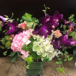 Purple orchids and pink hydrangeas in a square glass vase
