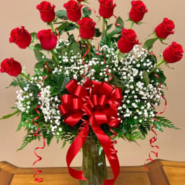 Red roses in a clear glass vase with baby's breath and a red bow