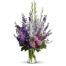 Tall arrangement of purple and white flowers with lavender roses in a clear glass vase