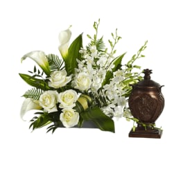 White roses and calla lilies with orchids in a low arrangement beside a bronze urn