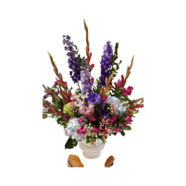 Tall mixed flower arrangement in a white vase with purple, pink, and blue blooms