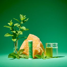 Mint sprigs in a glass vial with a salt rock, balm tube, and two small liquid vials