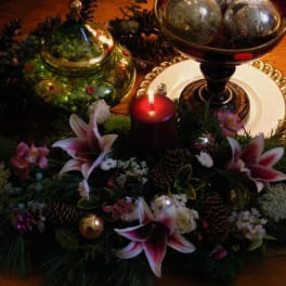Holiday centerpiece with lilies, a red candle, and decorative ornaments