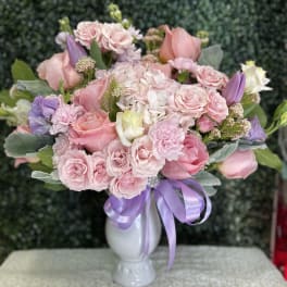 Pink and lavender bouquet in a white vase with a purple ribbon