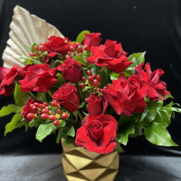 Red roses arranged in a gold geometric vase with berry accents
