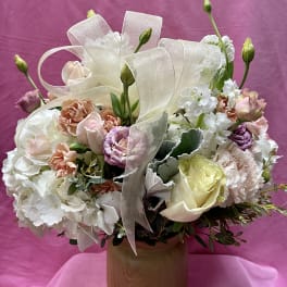 Pastel bouquet of roses, carnations, and white blooms in a wooden vase with ribbon