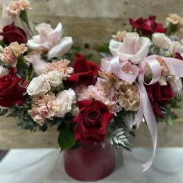 Red roses and pale pink carnations in a burgundy vase with a pink ribbon