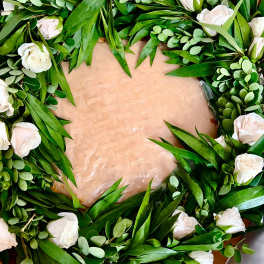 Wreath of white roses and greenery arranged in a circle on a flat base