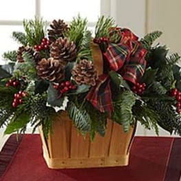 Holiday arrangement with pinecones, berries, and a plaid bow in a wooden basket