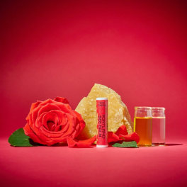 Red rose with lip balm, a crystal, and two small glass vials on a red background