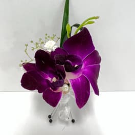 Purple orchid boutonniere with white filler flowers, ribbon, and pins on a white background