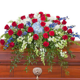 Red, white, and blue casket spray of mixed flowers on a wooden casket
