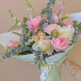 Pastel bouquet of pink, peach, and white flowers wrapped in pale paper