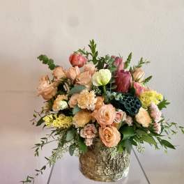 Peach and pink floral arrangement in a rustic bark-covered container