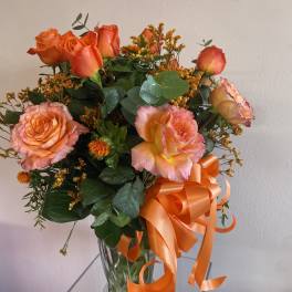 Orange and pink roses in a clear glass vase with an orange ribbon