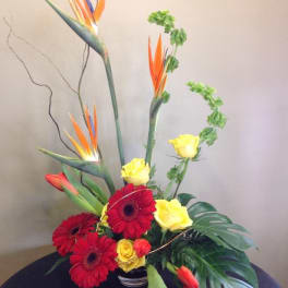 Tropical flower arrangement with red gerbera daisies and yellow roses in a vase