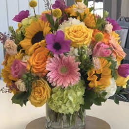 Colorful bouquet in a clear glass vase with roses, sunflowers, and gerbera daisies