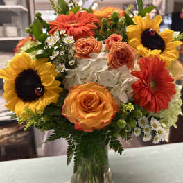 Bouquet of sunflowers, orange roses, and white hydrangeas in a glass vase