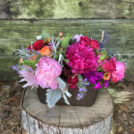 Mixed bouquet of pink, red, and orange flowers in a dark container
