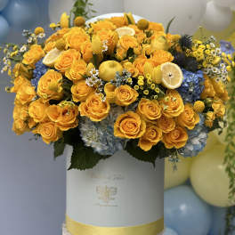 Yellow rose arrangement in a white hat box with blue hydrangeas and lemon slices