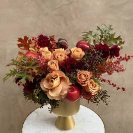 Peach roses and burgundy flowers in a gold vase with autumn leaves and berries