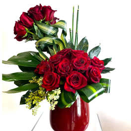 Red roses arranged in a red vase with striped ribbon accents