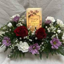 Floral arrangement with red roses, white and purple flowers, and a lit memorial candle