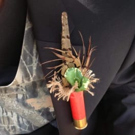 Small boutonniere with a red shotgun shell and green accent on dark fabric
