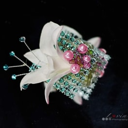 White floral corsage with pink and teal bead accents on a black background
