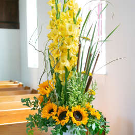 Tall yellow floral arrangement with sunflowers in a white pedestal vase