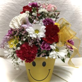 Mixed bouquet in a yellow smiley-face pot with a ribbon bow