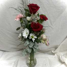 Red roses and mixed flowers in a clear glass vase with a patterned ribbon