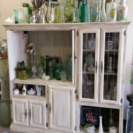 White cabinet filled with assorted glass vases and a few small floral pieces