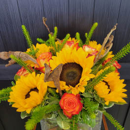 Sunflowers and orange roses arranged in a clear square vase