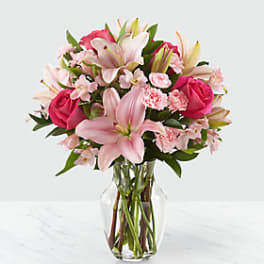 Pink lilies and roses arranged in a clear glass vase