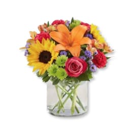 Colorful mixed bouquet in a clear glass vase with a sunflower and orange lily