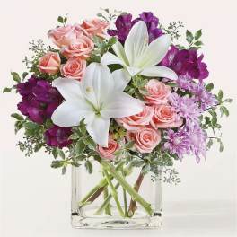 Pink roses and purple flowers with white lilies in a clear glass vase