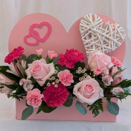 Pink roses and carnations arranged in a heart-shaped box with wicker hearts