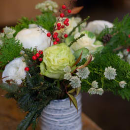 White and pale green floral arrangement in a white vase with red berry accents