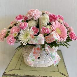 Pink and white flowers in a white wicker basket with a floral ribbon