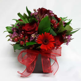 Red roses and a red gerbera daisy in a black vase with a red ribbon