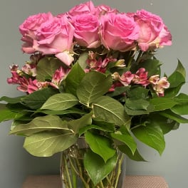 Pink roses and small pink flowers arranged in a clear glass vase.