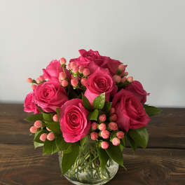 Compact arrangement of bright pink roses and pink berries in a clear glass vase