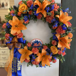 Circular floral wreath with orange lilies, roses, and blue flowers