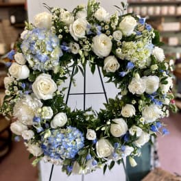 Large white floral wreath with blue accents on a stand